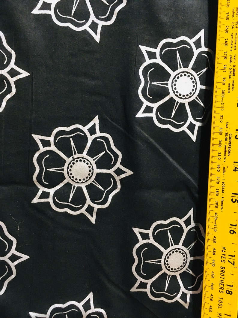 May include: Black fabric with a white repeating pattern of stylized flowers. The fabric is measured with a yellow ruler.