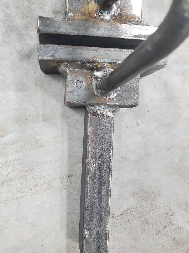 May include: Close-up of a metal tool with a heart-shaped mark. The tool is made of steel and has a rectangular shape. It appears to be a blacksmithing tool.