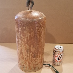 May include: A large, rusty, metal weight with a loop on top. The weight is about the size of a soda can.