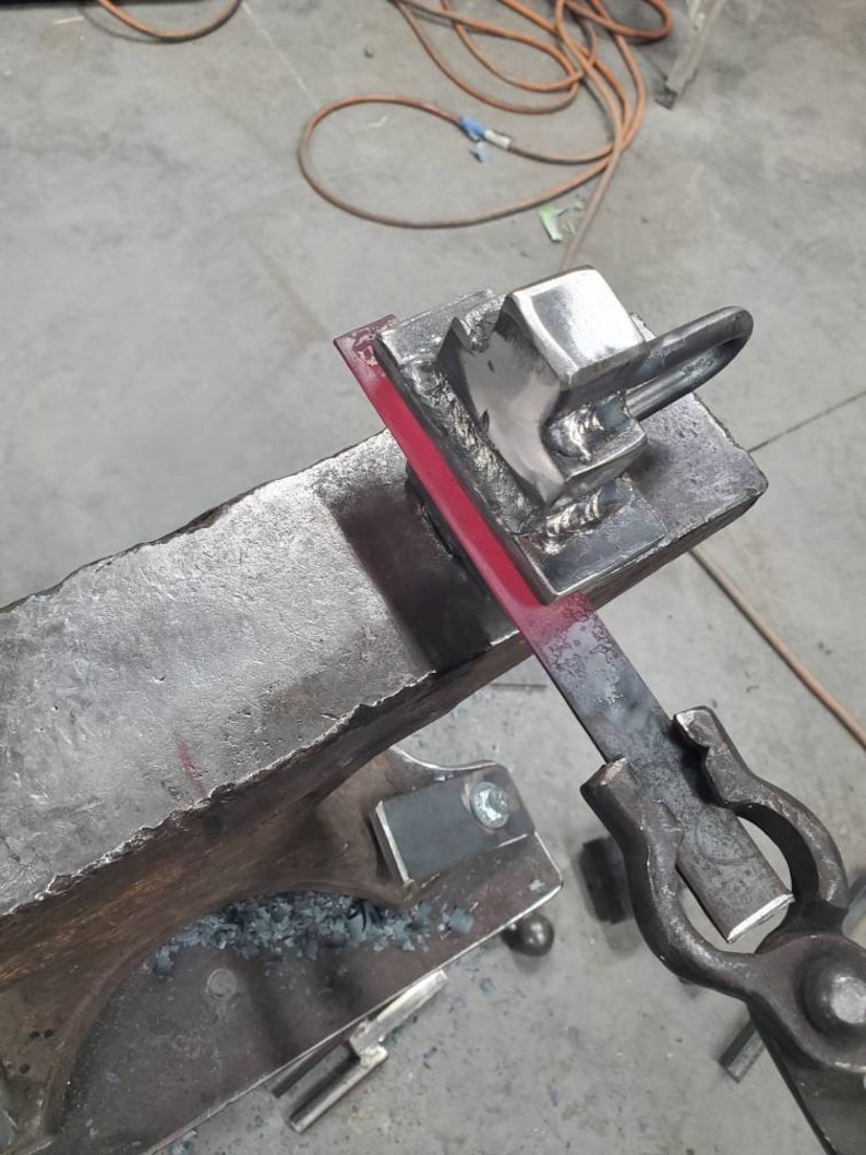 May include: A metal piece is being shaped on an anvil with a hammer. The metal is red hot and glowing. The anvil is made of iron and has a rough surface. The hammer is made of metal and has a wooden handle.