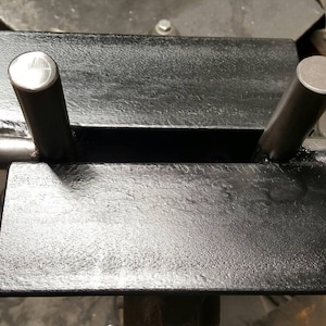 May include: A black metal barbell holder with two metal posts. The holder is designed to hold a barbell in place for weightlifting exercises.