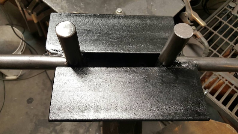 May include: A black metal barbell holder with two metal posts. The holder is designed to hold a barbell in place for weightlifting exercises.