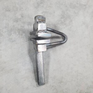 May include: A silver metal tool with a square head and a long handle. The tool has a loop on the side and is designed for tightening or loosening objects.