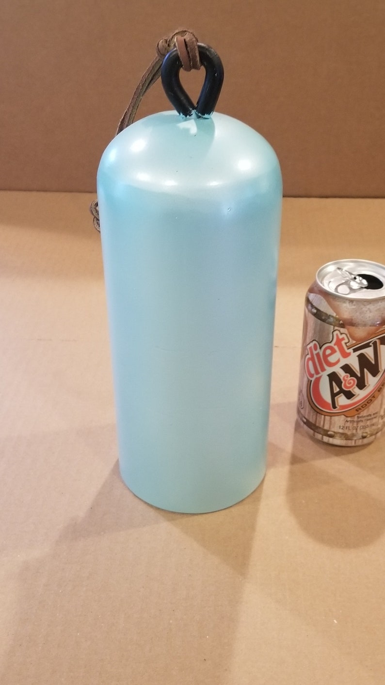 Może przedstawiać: Dzwonek ceramiczny w jasnoniebieskim kolorze z czarnym metalowym uchwytem i brązowym sk&oacute;rzanym paskiem. Dzwonek jest mniej więcej wielkości standardowej puszki napoju.