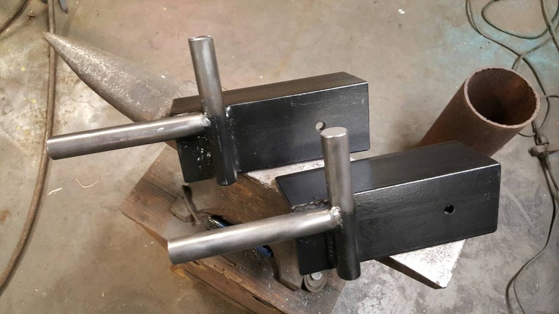May include: Two black metal brackets with welded steel arms. The brackets are sitting on a metal anvil.