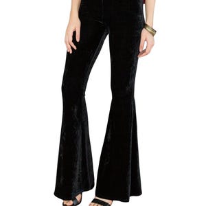 May include: Black velvet flared pants. The pants have a high waist and a wide flare from the knee down. The fabric has a soft, textured appearance. The pants are worn with black sandals.