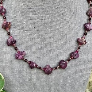 May include: A necklace made with small, irregular, dark pink ruby beads and smaller, round, dark pink beads.