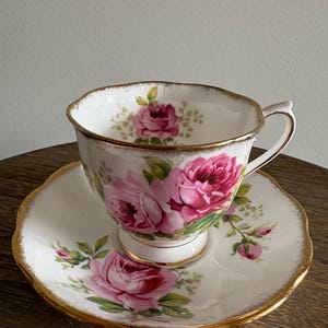 May include: A white teacup and saucer with a pink rose floral pattern and gold trim.