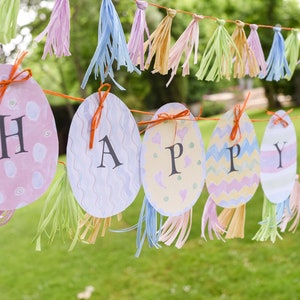 May include: A colorful banner with the word "HAPPY" spelled out on pastel-colored egg shapes. Each egg has a different pattern and is decorated with orange ribbon. The banner is strung with light blue, pink, and yellow tassels.