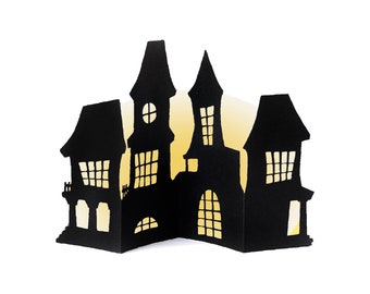 May include: Black paper cut-out of a haunted house with windows and a door. The house is silhouetted against a yellow background.