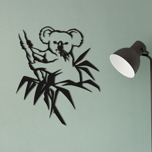 May include: Black metal wall art featuring a koala bear climbing a bamboo tree. The koala is in a sitting position with its arms wrapped around the bamboo.