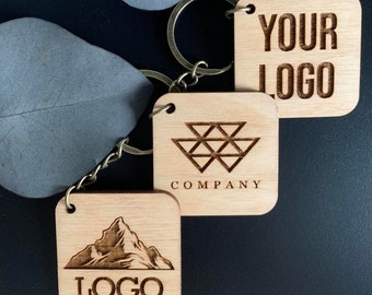 May include: Three wooden keychains with different designs. The first keychain has a mountain range and the text "LOGO". The second keychain has a geometric design and the text "COMPANY". The third keychain has the text "YOUR LOGO".