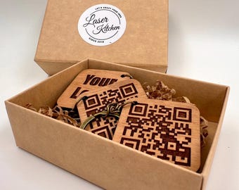 May include: A set of three wooden keychains in a brown cardboard box. The keychains feature a QR code and the text "Your Logo" engraved on the wood. The box has a sticker with the text "Laser Kitchen" and "Let's Craft Your Idea Since 2018".