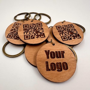 Può includere: Un set di portachiavi in legno con un codice QR inciso a laser e il testo "Your Logo". I portachiavi sono marroni e hanno un anello in ottone.