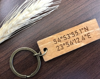 May include: Wooden keychain with a brown leather loop and engraved coordinates: 54°53'55.1"N 23°54'12.4"E
