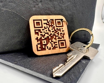 May include: A wooden keychain with a laser-engraved QR code. The keychain is attached to a silver key and a gold-colored key ring.