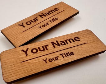 May include: Two rectangular wooden name tags with rounded corners. Each tag features the laser-engraved text "Your Name" on the top line and "Your Title" on the bottom line, separated by a horizontal line. The wood has a natural light brown grain.