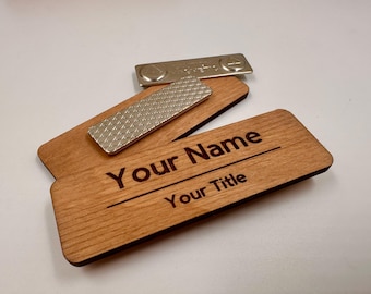 May include: Two rectangular wooden name badges with rounded corners. The front badge features the laser-engraved text "Your Name" and "Your Title" with a horizontal line. A silver-colored magnetic fastener with a textured surface is attached.