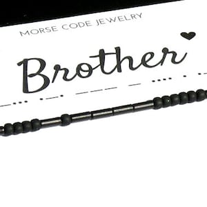 Pode incluir: Pulseira de contas pretas com a palavra "Brother" em it&aacute;lico e o c&oacute;digo Morse correspondente abaixo. A pulseira est&aacute; em um cart&atilde;o branco com as palavras "Morse Code Jewelry" no topo.