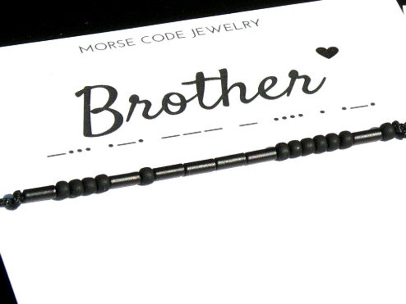Pode incluir: Pulseira de contas pretas com a palavra "Brother" em it&aacute;lico e o c&oacute;digo Morse correspondente abaixo. A pulseira est&aacute; em um cart&atilde;o branco com as palavras "Morse Code Jewelry" no topo.