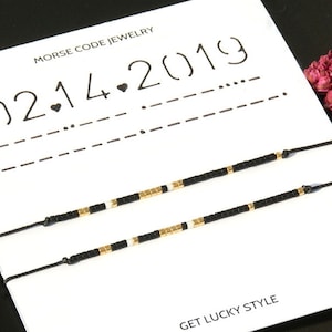 Peut inclure: Deux bracelets en cordon noir avec des perles dorées et blanches. Les bracelets sont sur une carte blanche avec le texte "Morse Code Jewelry (02.14.2019)" et "Get Lucky Style".
