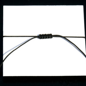 Pode incluir: Um bracelete de cord&atilde;o preto com um n&oacute; no centro.