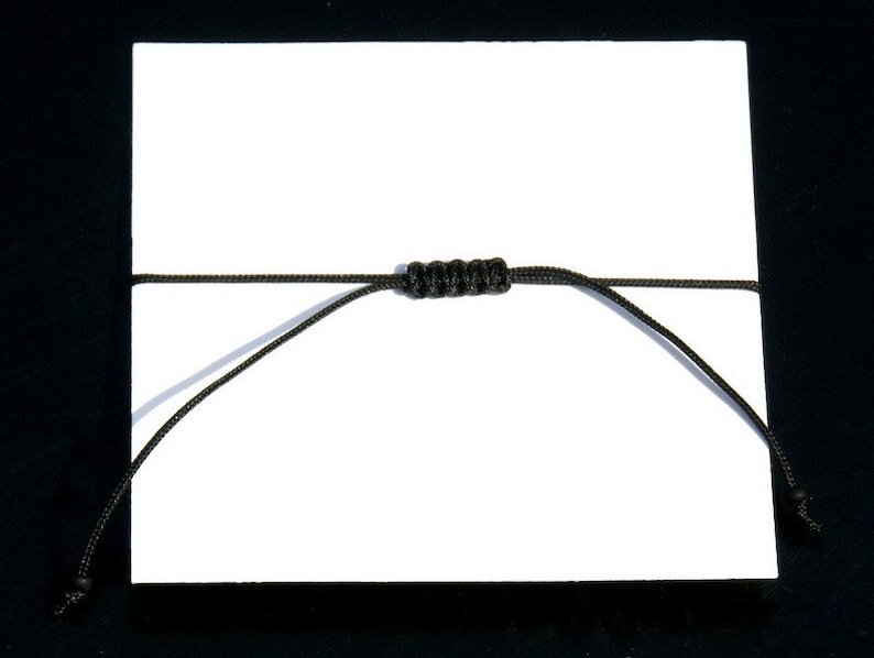 Pode incluir: Um bracelete de cord&atilde;o preto com um n&oacute; no centro.