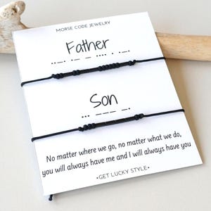 May include: A white card with the words "Father" and "Son" above two black beaded bracelets. The bracelets are in Morse code. The card also has the text "No matter where we go, no matter what we do, you will always have me and I will always have you."