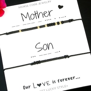 May include: A white card with black string bracelets and black beads. The card reads "Morse Code Jewelry" and has the words "Mother" and "Son" written in black ink. The card also has the text "Our Love is forever..." and "Get Lucky Style."