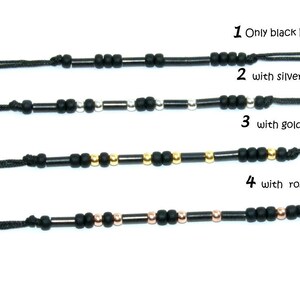 Pode incluir: Quatro pulseiras de cord&atilde;o preto com contas de diferentes cores. A primeira pulseira tem apenas contas pretas. A segunda pulseira tem contas pretas com contas prateadas. A terceira pulseira tem contas pretas com contas douradas. A quarta pulseira tem contas pretas com contas de ouro rosa.