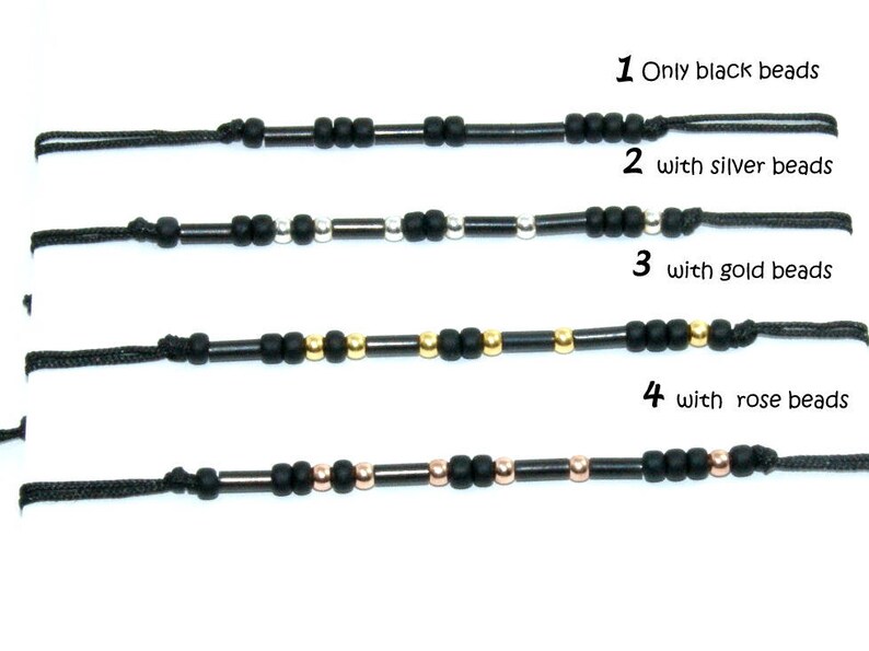 Pode incluir: Quatro pulseiras de cord&atilde;o preto com contas de diferentes cores. A primeira pulseira tem apenas contas pretas. A segunda pulseira tem contas pretas com contas prateadas. A terceira pulseira tem contas pretas com contas douradas. A quarta pulseira tem contas pretas com contas de ouro rosa.