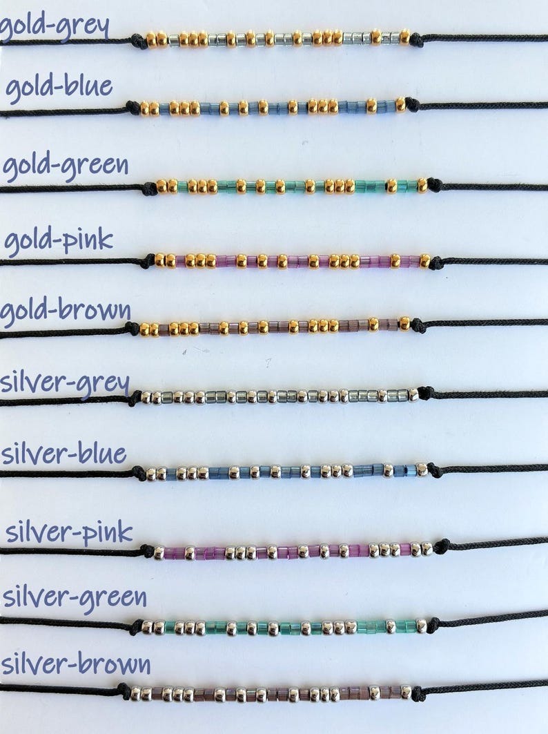 May include: A collection of beaded bracelets in various color combinations, including gold and silver beads with grey, blue, green, pink, and brown accents. Each bracelet is strung on a black cord.
