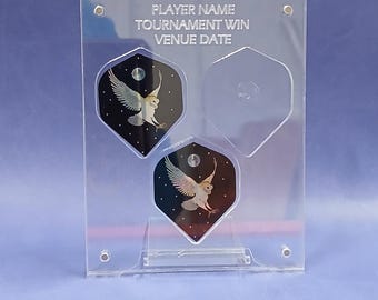 May include: A clear acrylic display case for darts with three slots. The case has a white background with the text "PLAYER NAME, TOURNAMENT WIN, VENUE DATE". The slots are filled with three darts with a black background and a white owl design.
