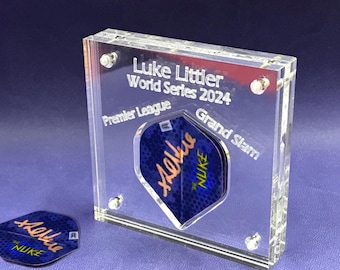 May include: A clear acrylic display case with a dart inside. The case has the text "Luke Littler World Series 2024 Premier League Grand Slam" engraved on it.