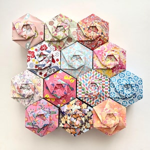 May include: A collection of eleven hexagonal origami boxes arranged in a cluster. Each box features a unique folded paper design with various floral, geometric, and traditional patterns in colors including pink, blue, yellow, red, and navy.