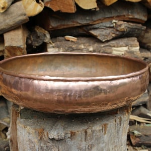 May include: A large, round copper bowl with a hammered finish. The bowl is sitting on a wooden stump.