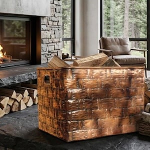 May include: A rectangular copper-toned metal storage bin with a woven-style textured surface and side handles, positioned in a room with a stone fireplace, large windows, and stacks of firewood logs arranged on the floor and in the hearth area.