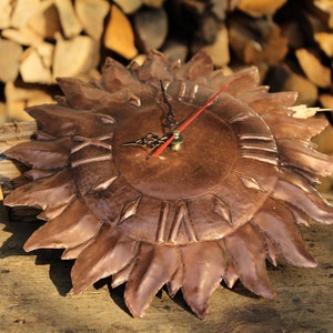 May include: A copper clock shaped like a sun with Roman numeral markings on the face. The clock hands are red and black.