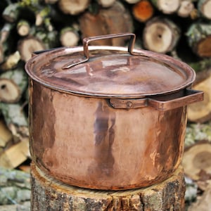以下が含まれることがあります： 蓋と取っ手が付いた大きな銅製の鍋。鍋は木の切り株の上に置かれています。