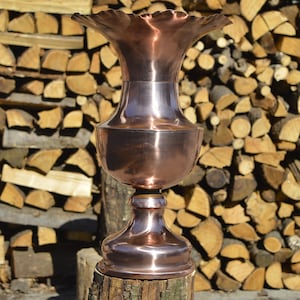 May include: A copper vase with a wide, scalloped rim and a round base. The vase is standing on a wooden stump.