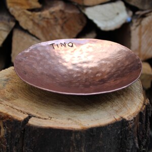 May include: A hammered copper bowl with the name "Tino" inscribed on the inside. The bowl is sitting on a wooden stump.