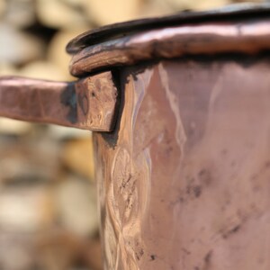 May include: A copper pot with a handle and a hammered finish. The pot is slightly tarnished and has a rustic look.