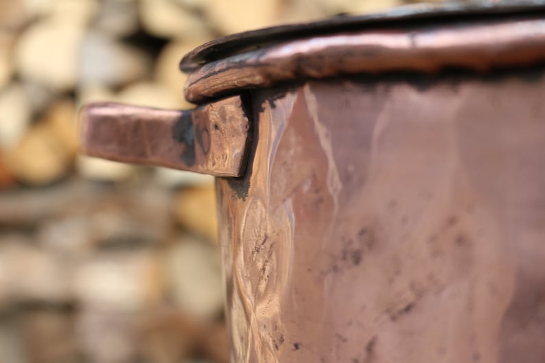 May include: A copper pot with a handle and a hammered finish. The pot is slightly tarnished and has a rustic look.