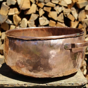 Peut inclure: Une grande marmite en cuivre avec une finition martelée et une seule poignée. La marmite est posée sur une surface en bois.