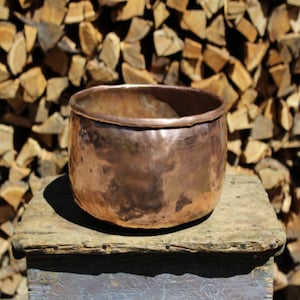 May include: A hammered copper bowl with a rounded bottom and a slightly flared rim. The bowl is sitting on a wooden surface.