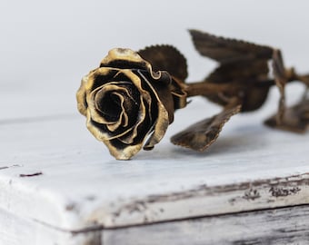 May include: A gold metal rose with a black centre, lying on a white wooden surface.