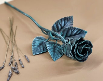 May include: A teal blue metal rose with leaves, lying on a brown surface. A bundle of dried lavender is in the lower left corner of the image.