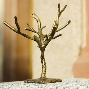 May include: A gold metal tree-shaped ring holder with a twisted trunk and branches. The holder is on a gray surface.