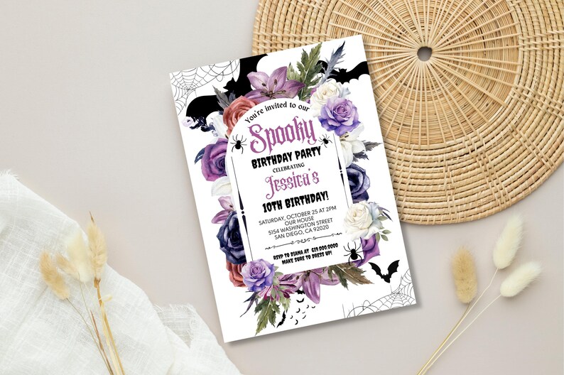 May include: A white invitation card with a purple, black, and white floral design. The text on the card reads "You're invited to our Spooky Birthday Party Celebrating Jessica's 10th Birthday!"  The invitation includes the date, time, and location of the party.