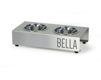 May include: Stainless steel double dog bowl stand with the name "BELLA" engraved on the front.